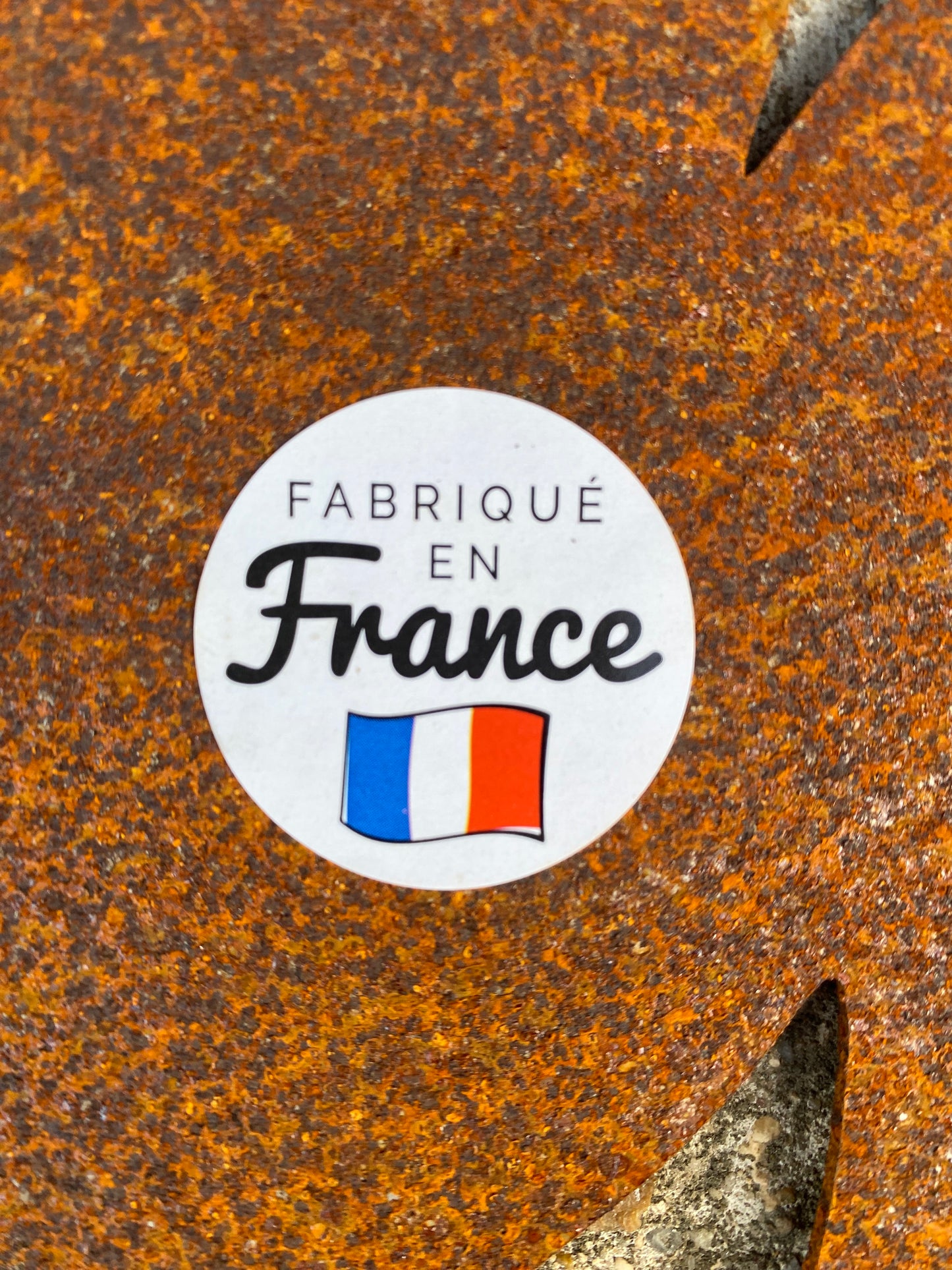 Étiquette ronde "FABRIQUÉ EN France" posée sur une surface rouillée orange.