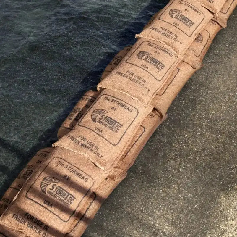 Sacs étanches en carton imprimé “Stormbag” alignés sur le sol, destinés à l’inondation et au stockage d’eau pour le jardin.